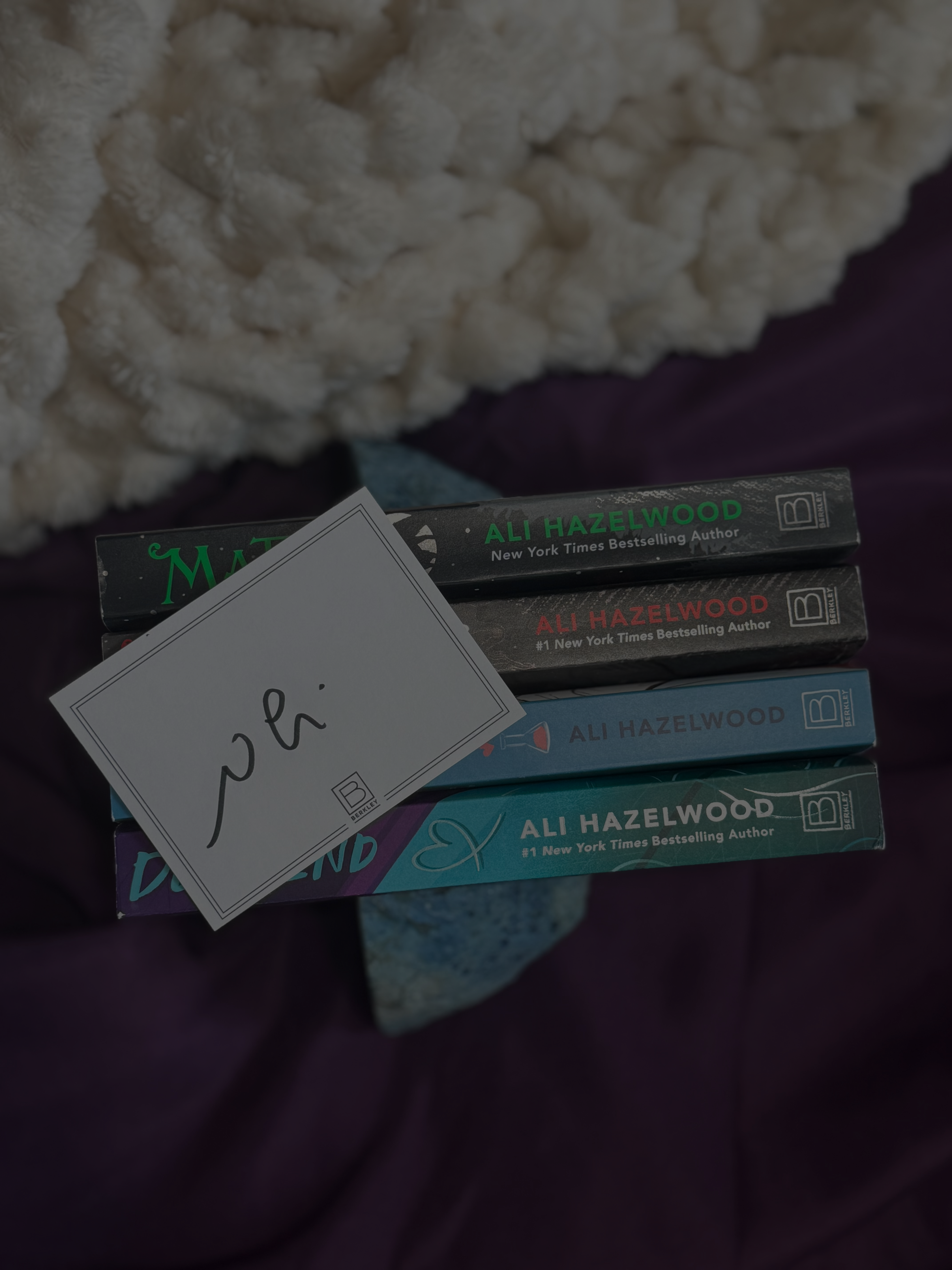 Stack of books by Ali Hazelwood with a white card on a textured surface